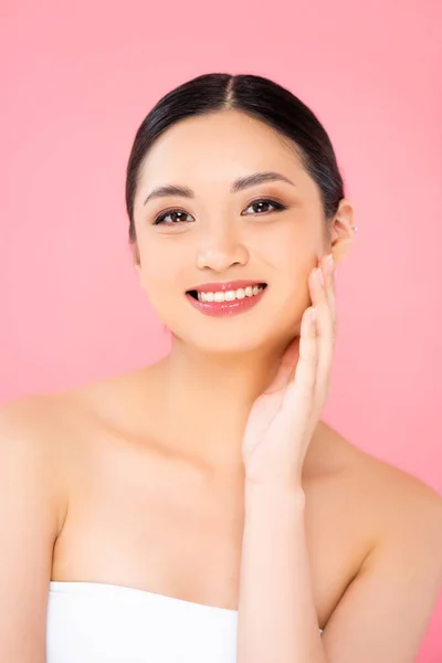 Young asian woman touching face and looking at camera isolated on pink — Stock Photo