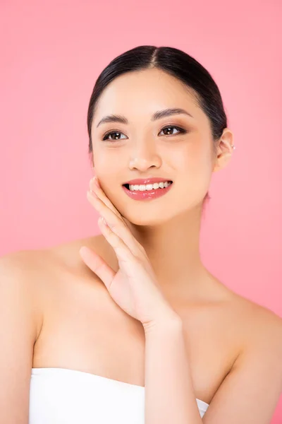 Brunette asian woman looking away while touching face isolated on pink — Stock Photo