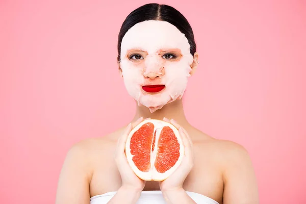 Young asian woman in face mask holding half of ripe grapefruit isolated on pink — Stock Photo