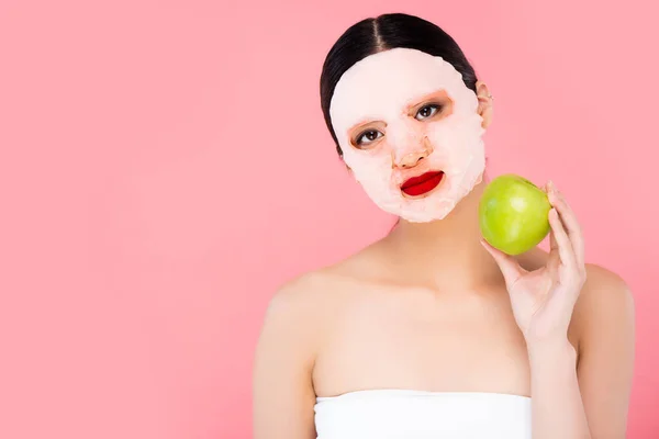Ásia mulher no rosto máscara segurando verde maçã enquanto olhando para câmera isolado no rosa — Fotografia de Stock