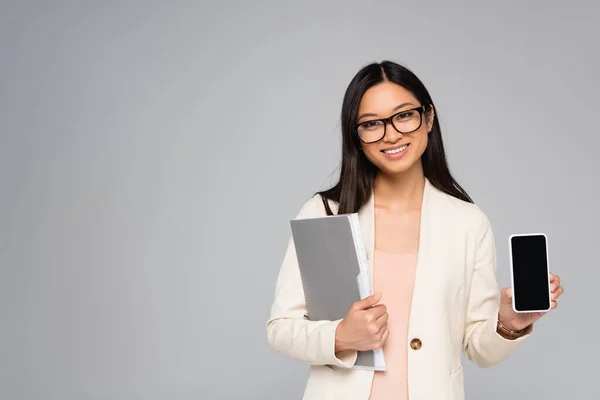 Asiatische Geschäftsfrau mit Brille hält Ordner und Smartphone mit leerem Bildschirm isoliert auf grau — Stockfoto