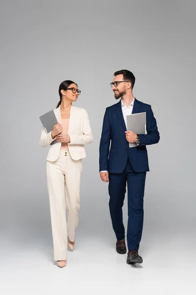 Interracial couple of business partners holding folders and looking at each other while walking on grey — Stock Photo