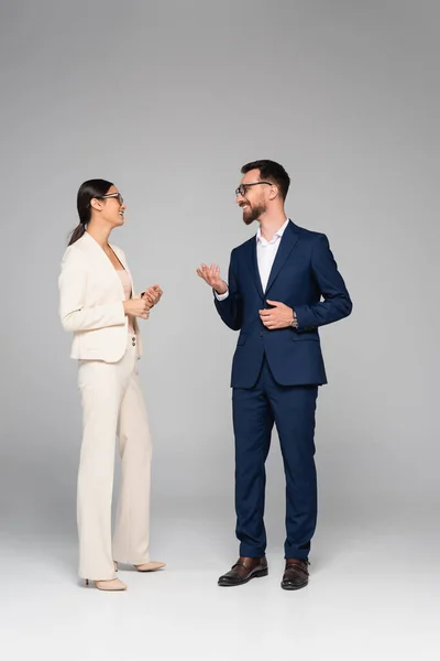 Vista completa de colegas de negocios interracial en ropa formal hablando y haciendo gestos en gris - foto de stock