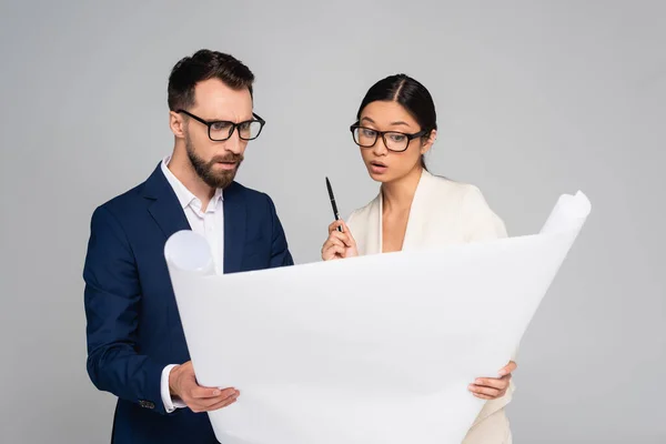 Thoughtful interracial couple of business partners in eyeglasses looking at white placard isolated on grey — Stock Photo