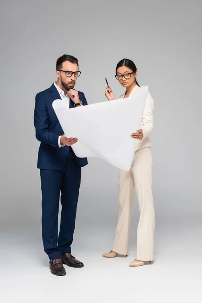 Shocked businessman and asian businesswoman looking at white placard on grey — Stock Photo