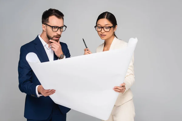 Nachdenkliche interrassische Geschäftspartner blicken auf weißes Plakat isoliert auf grau — Stockfoto