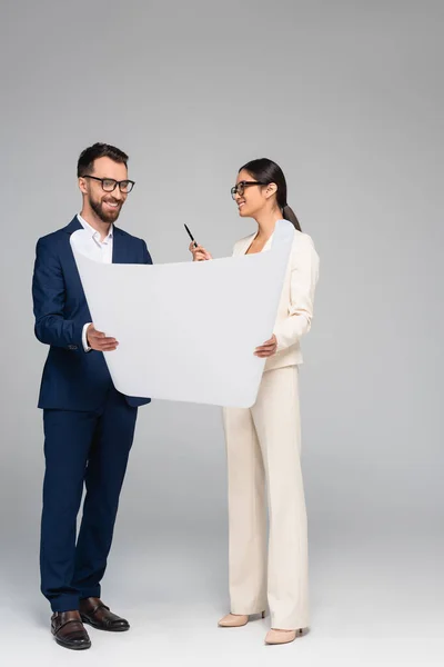 Asian businesswoman talking to business partner while holding white paper on grey — Stock Photo