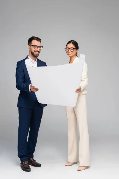 Vue complète du couple interracial d'hommes d'affaires regardant le papier blanc sur gris — Photo de stock