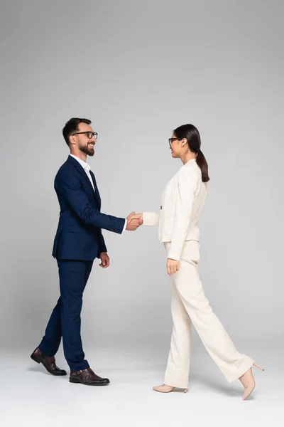 Vista completa de colegas de negocios interracial en ropa formal estrechando las manos en gris - foto de stock