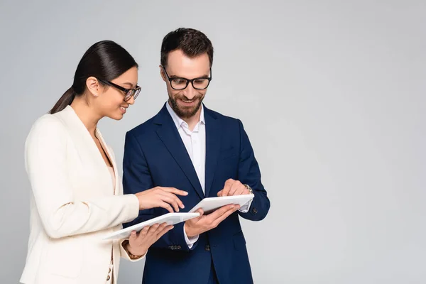 Coppia interrazziale di colleghi di lavoro in blazer e occhiali utilizzando tablet digitali isolati su grigio — Foto stock