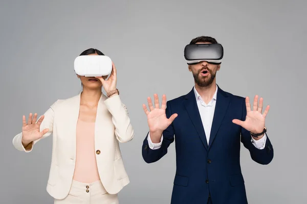 Excited businesspeople in vr headsets gesturing like touching something isolated on grey — Stock Photo