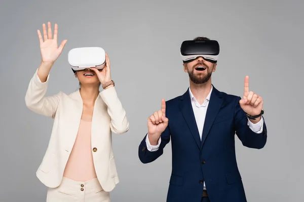 Aufgeregte Geschäftspartner in vr-Headsets gestikulieren, als würden sie etwas Isoliertes auf Grau berühren — Stockfoto