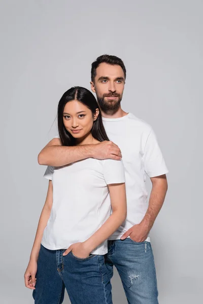 Jovem casal interracial em camisetas brancas posando isolado no cinza — Fotografia de Stock