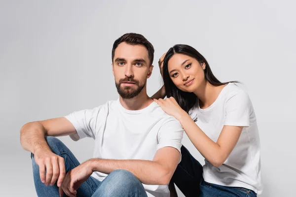 Joven asiático mujer mirando a cámara mientras sentado cerca novio aislado en blanco - foto de stock