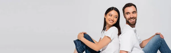 Horizontales Konzept eines jungen gemischtrassigen Paares in weißen T-Shirts, das Rücken an Rücken isoliert auf weiß sitzt — Stockfoto