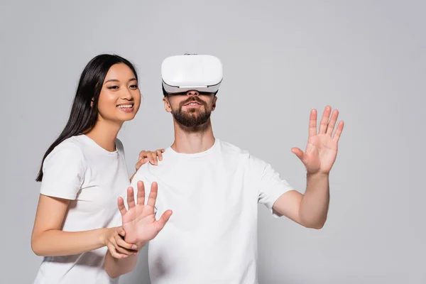 Brünette asiatin berühren aufgeregt freund gestikulierend im vr headset auf grau — Stockfoto