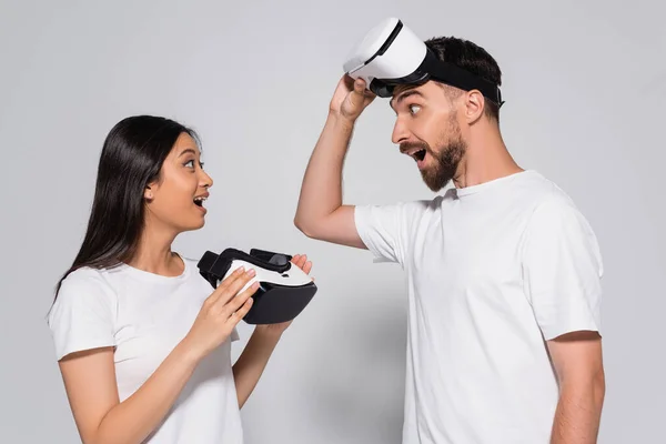 Junge asiatische Frau in weißem T-Shirt mit vr Headset, während sie aufgeregten Mann auf weiß ansieht — Stockfoto