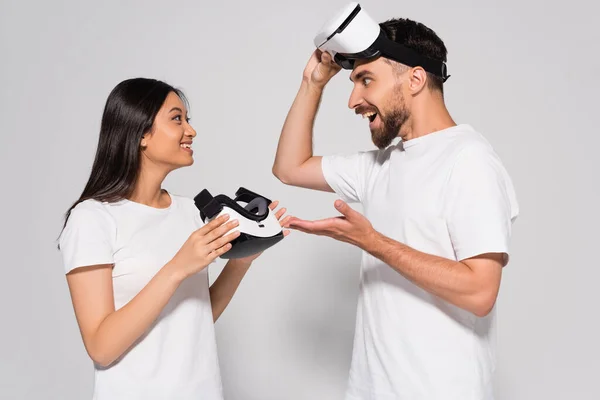Excited man talking to brunette asian woman while touching vr headset on white — Stock Photo
