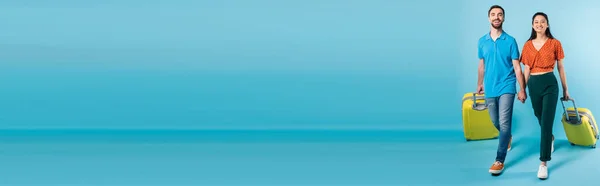Заголовок веб-сайту міжрасової пари туристів тримає руки під час прогулянки з валізами на синьому — стокове фото