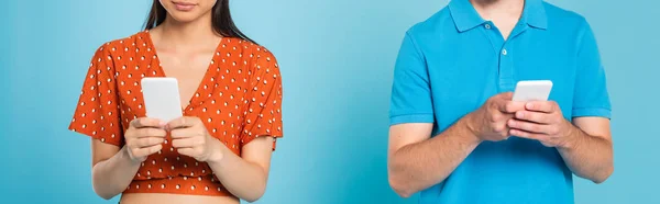 Обрізаний вид жінки в червоній блузці і чоловіка в футболці поло з використанням смартфонів на синій, панорамній орієнтації — стокове фото