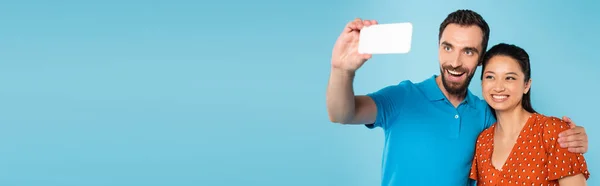 Horizontales Bild eines bärtigen Mannes, der ein Selfie mit einer brünetten Asiatin macht, isoliert auf blauem Grund — Stockfoto