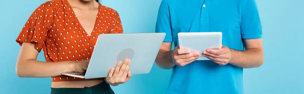 Vue partielle de la femme en chemisier rouge à l'aide d'un ordinateur portable près de l'homme avec tablette numérique sur bleu, culture horizontale — Photo de stock