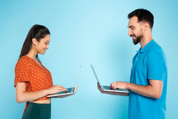 Side view of asian woman in red blouse and man in polo t-shirt using laptops on blue — Stock Photo