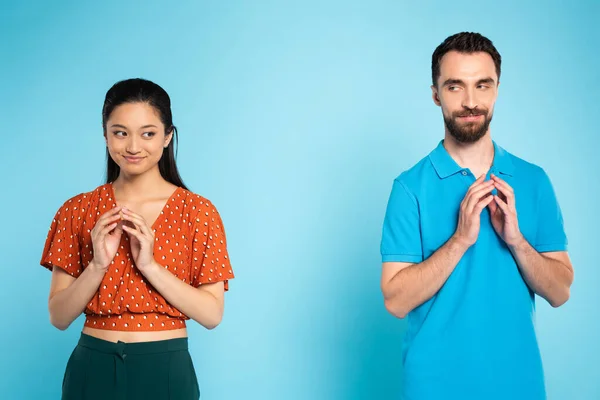 Astuto asiatico donna in rosso camicetta e ingannevole uomo in polo t-shirt gesturing con unito dita su blu — Foto stock