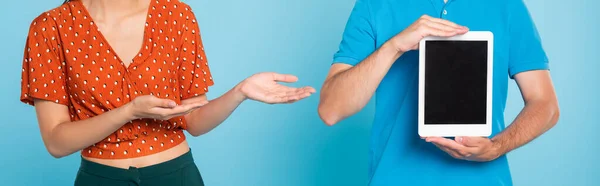 Vue recadrée de la femme en chemisier rouge pointant avec les mains à l'homme tenant tablette numérique avec écran blanc sur bleu, vue panoramique — Photo de stock