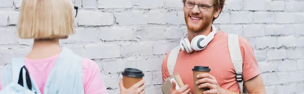 Panoramic shot of students holding paper cups near brick wall — Stock Photo