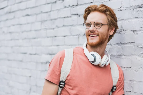 Redhead student in glasses and wireless headphones looking away — Stock Photo