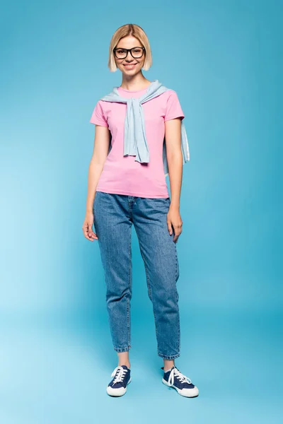 Blonde student in glasses looking at camera while standing on blue — Stock Photo