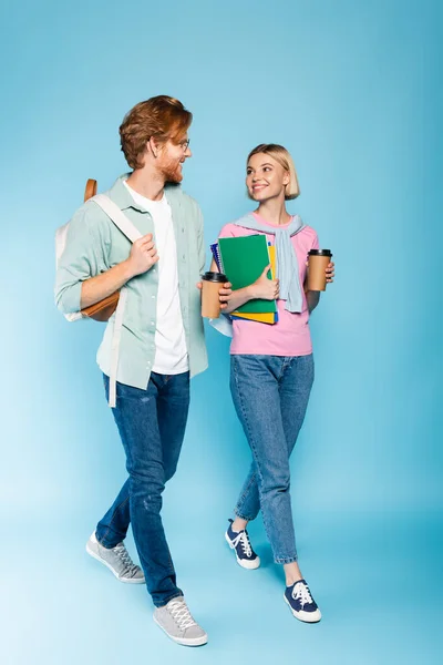 Young students holding coffee to go while walking on blue — Stock Photo