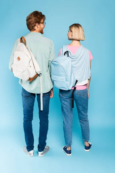 Back view of young students with backpacks standing on blue — Stock Photo