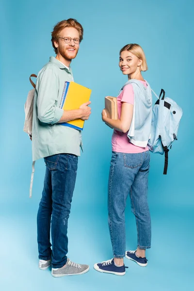 Студенты с рюкзаками, держащие в руках тетради и книги, стоя на синем — стоковое фото