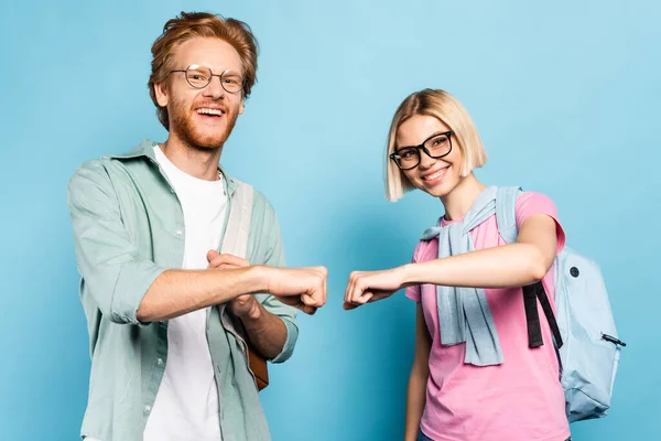 Young students in glasses looking at camera and fist bumping on blue — Stock Photo