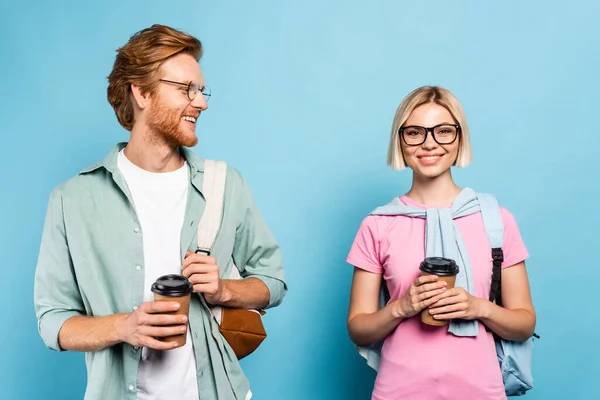 Jóvenes estudiantes en gafas sosteniendo vasos de papel en azul — Stock Photo