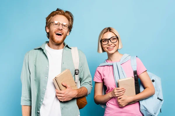 Схвильовані молоді студенти в окулярах тримають книги на синьому — стокове фото