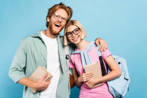 Rothaarige Mann und blonde Frau halten Bücher und umarmen sich auf blau — Stockfoto