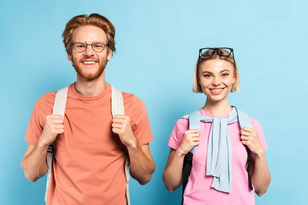 Redhead and blonde students with backpacks looking at camera on blue — Stock Photo