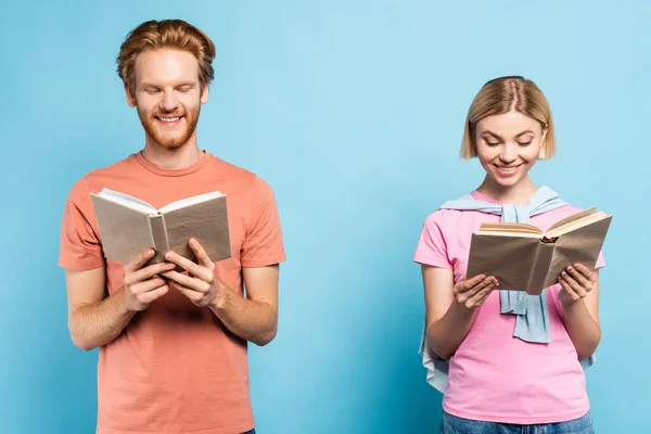 Young redhead and blonde students reading books on blue — Stock Photo