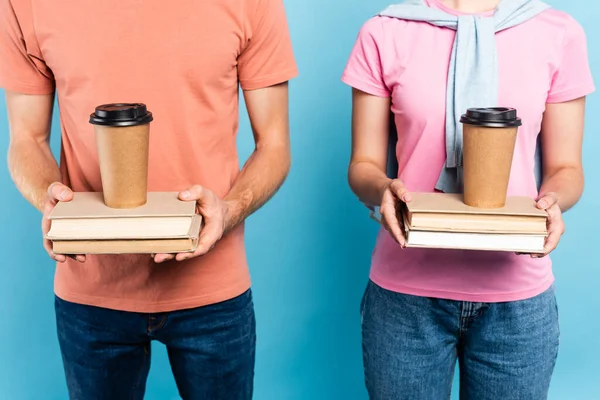 Cropped view of students holding books with coffee to go on blue — Stock Photo