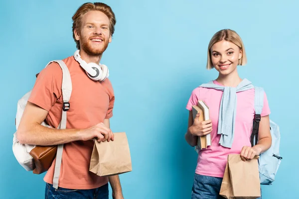Jeunes étudiants avec des sacs à dos tenant des sacs en papier sur bleu — Photo de stock