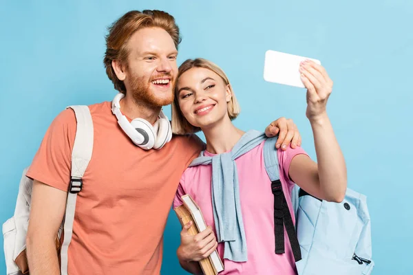 Selective focus of students with backpacks taking selfie on blue — Stock Photo