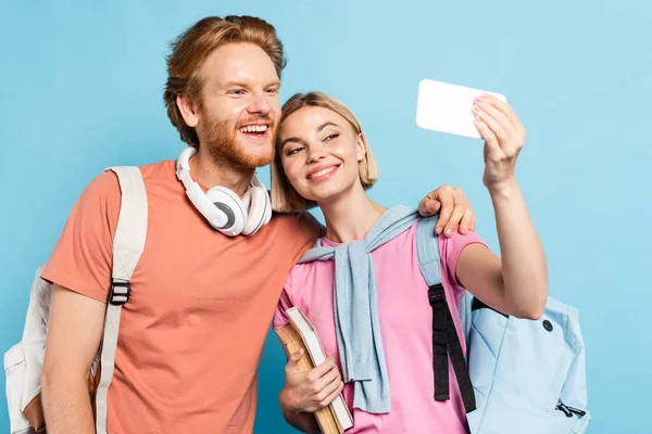 Foco seletivo de estudantes com mochilas tirando selfie no azul — Fotografia de Stock