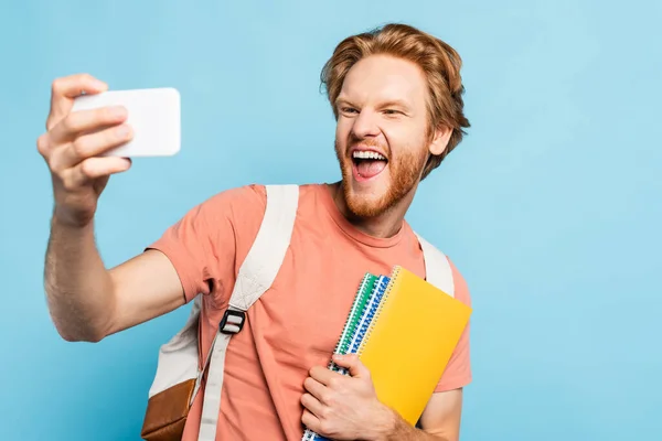 Foyer sélectif de l'élève excité tenant des carnets et de prendre selfie sur bleu — Photo de stock