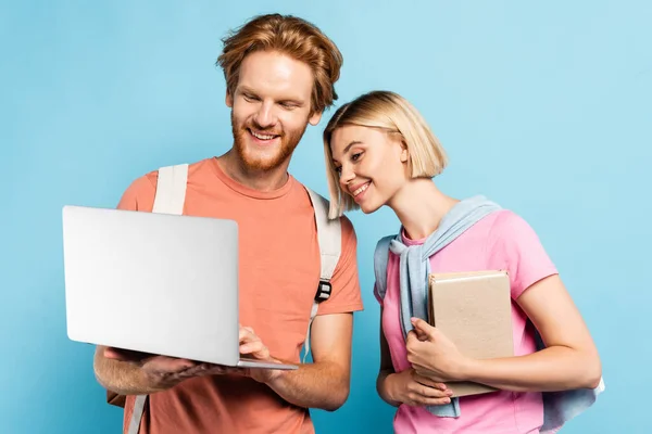 Redhead and blonde students looking at laptop on blue — Stock Photo