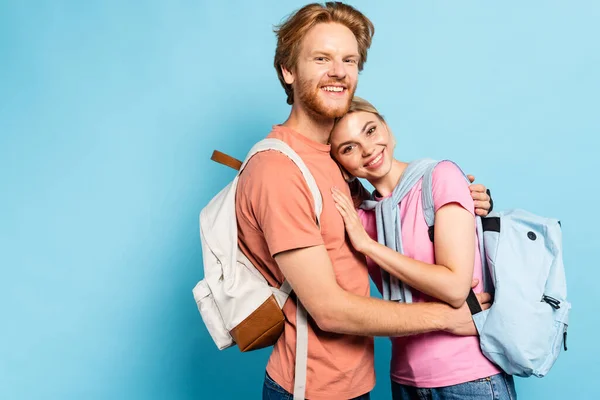Bärtige Studentin umarmt blonden Freund auf blau — Stockfoto