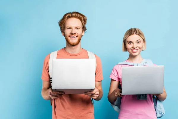 Redhead and blonde students holding laptops on blue — Stock Photo