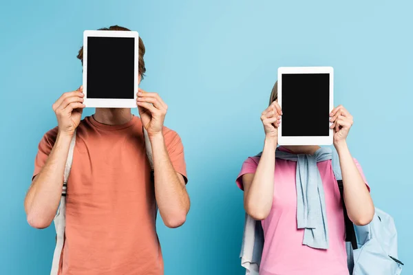 Jovens estudantes cobrindo rostos enquanto segurando tablets digitais com tela em branco em azul — Fotografia de Stock